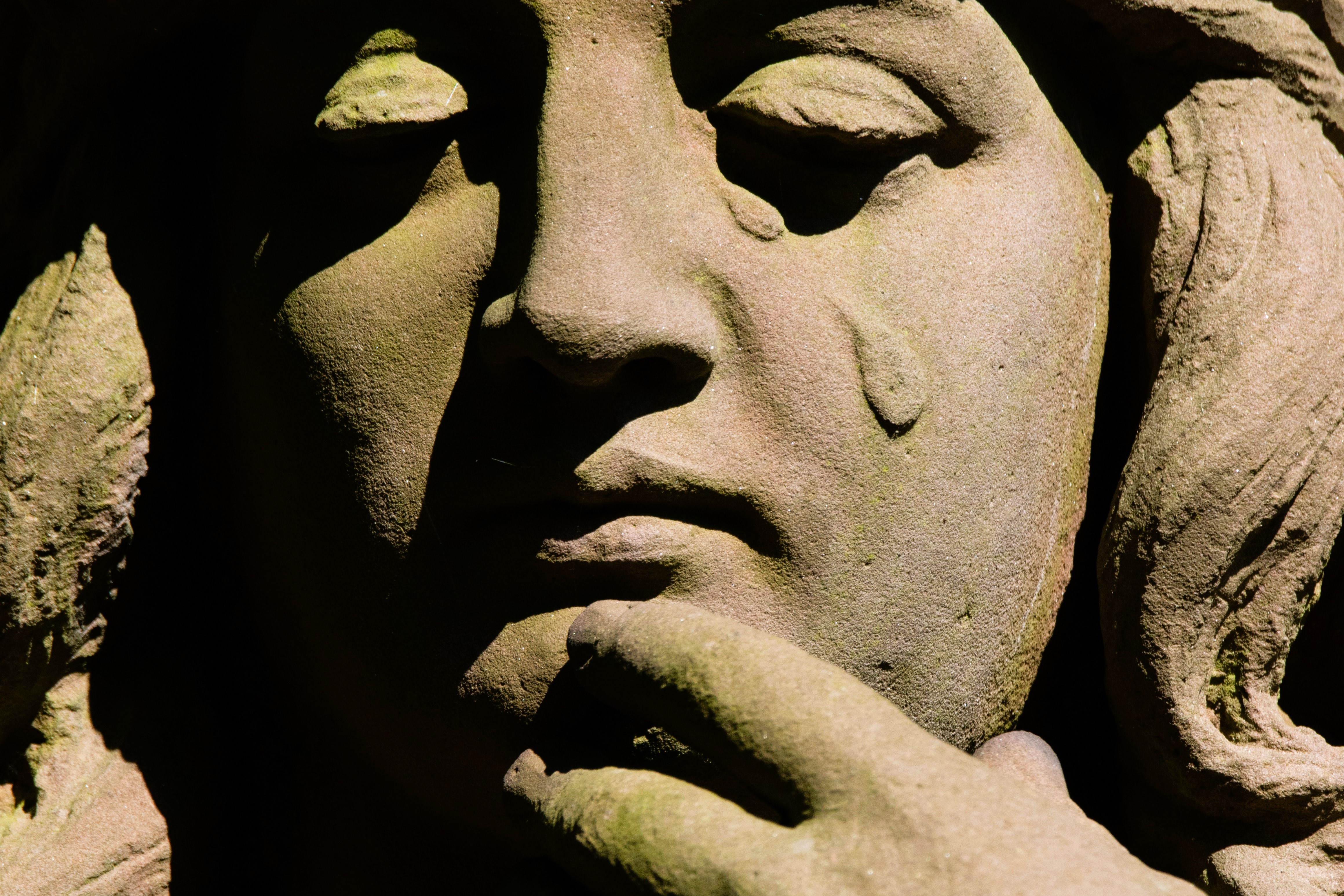 A stone statue's face depicts a falling tear.