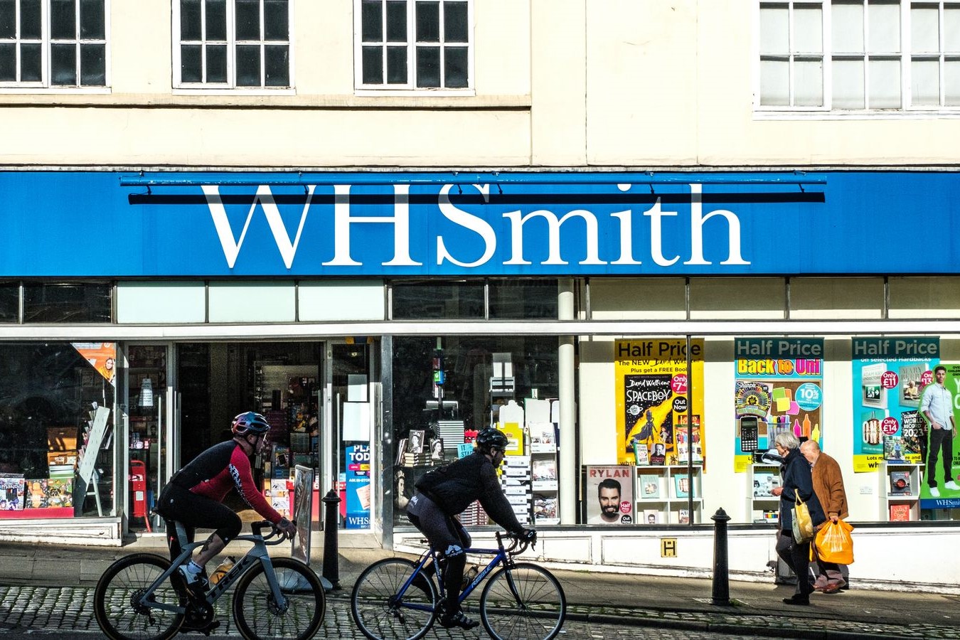 Cyclists and pedestrians pass in front of a WH Smith store front.