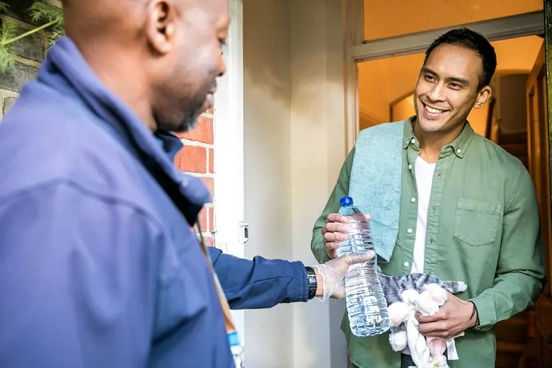 On a doorstep a man hands a bottle of water to another man.