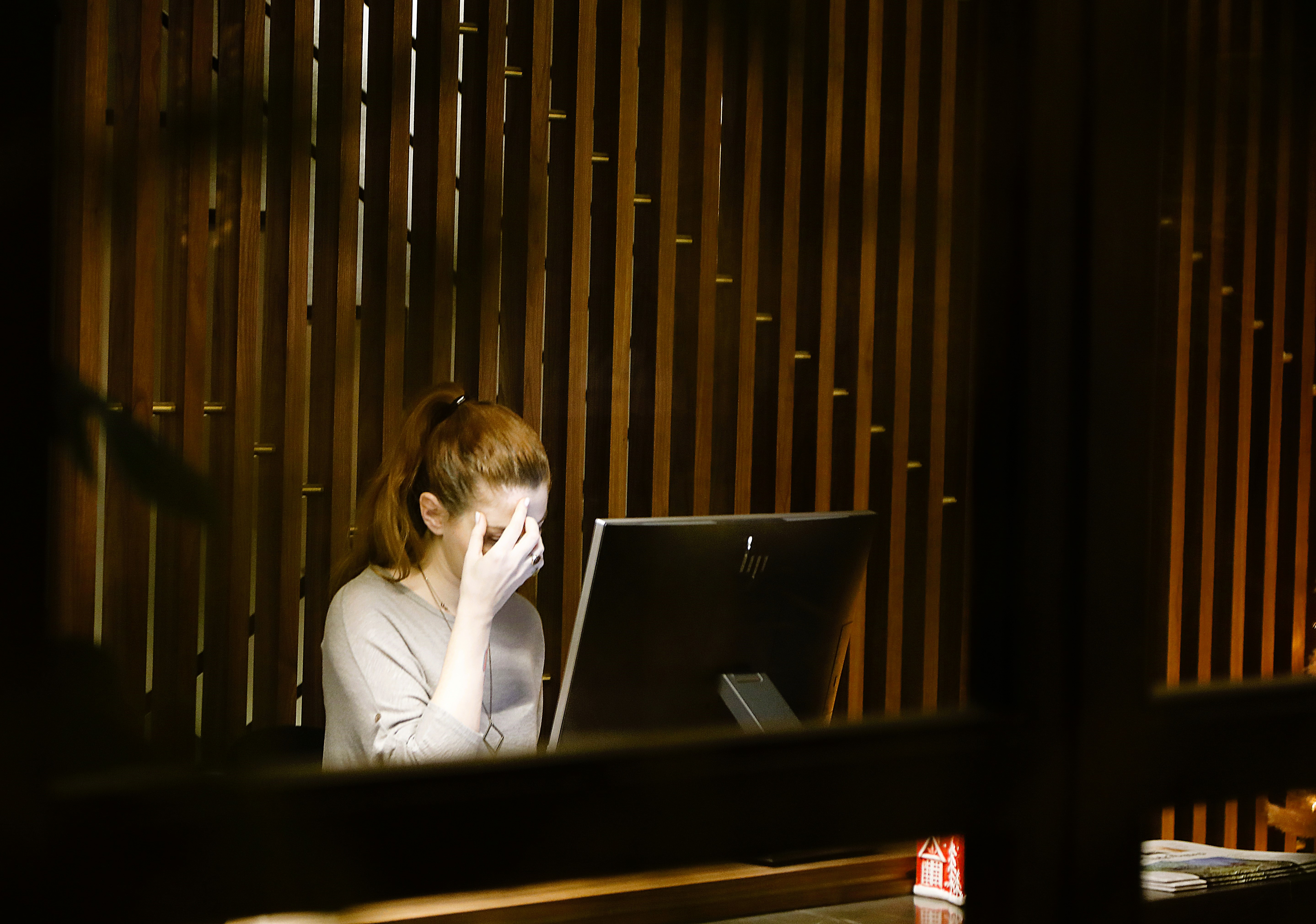 A woman rubs her face in worry, while siting at a screen.