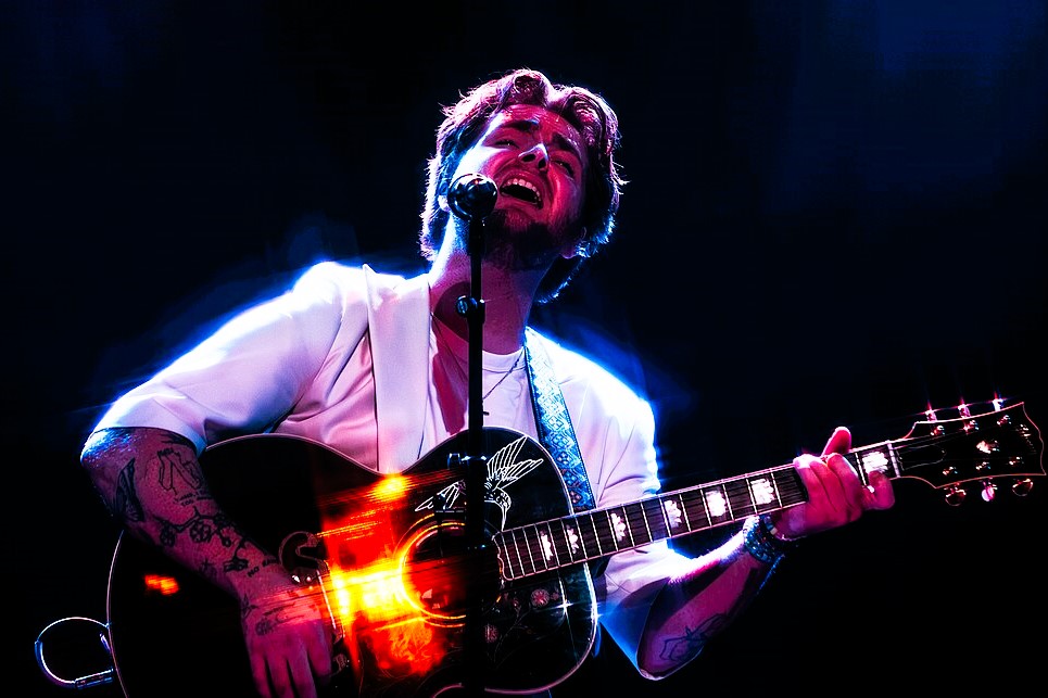 A singer holding a guitar raises his head with closed eyes.