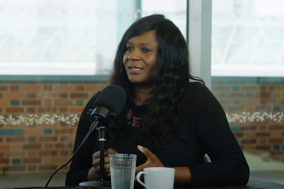 A podcast guest sits in front of a mic talking and gesturing with her hands.