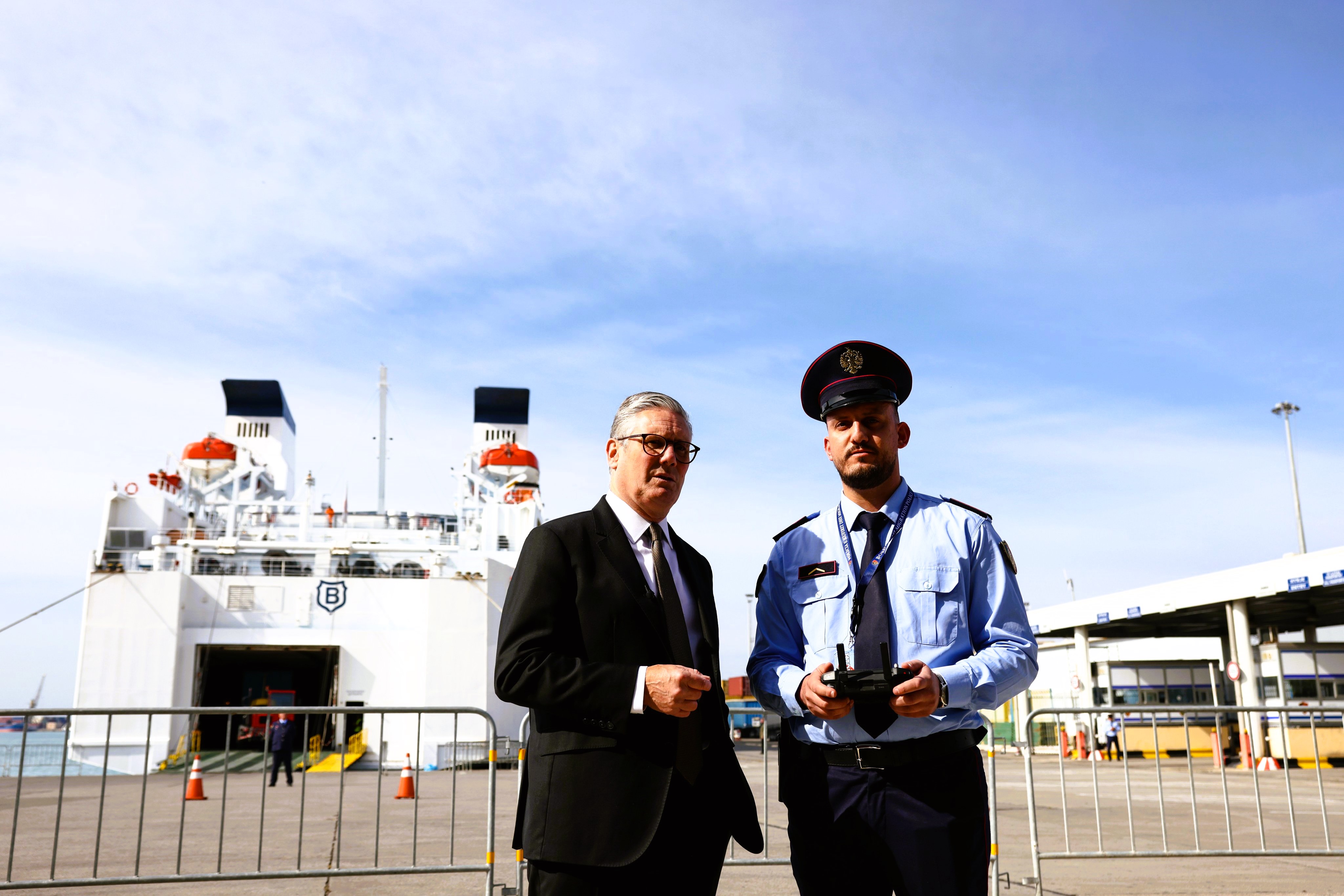 A prime minister stands next to an Albanian police officer in front of a ferry.