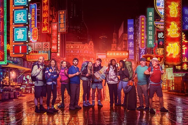 Contestants in Race Across the world stand in front of neon-lit Chinese street scene