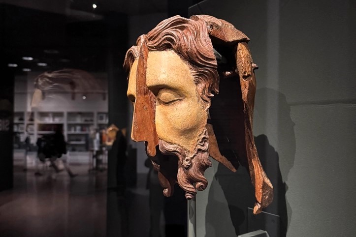 A split wooden sculpted head stands in an exhibition.