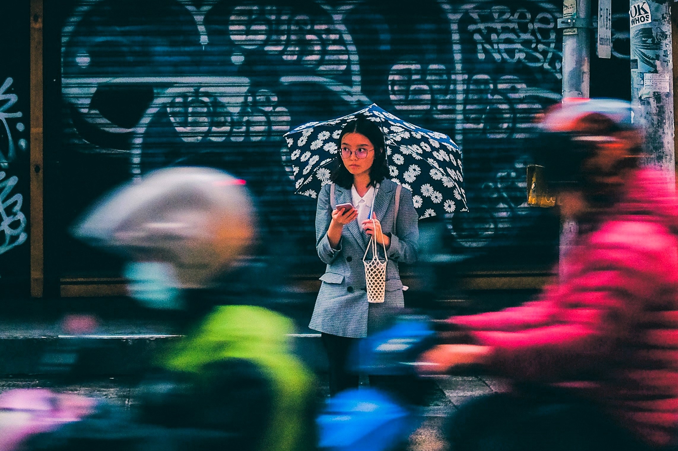 A woman stands across a busy roads, looking up from her phone in a sad way.