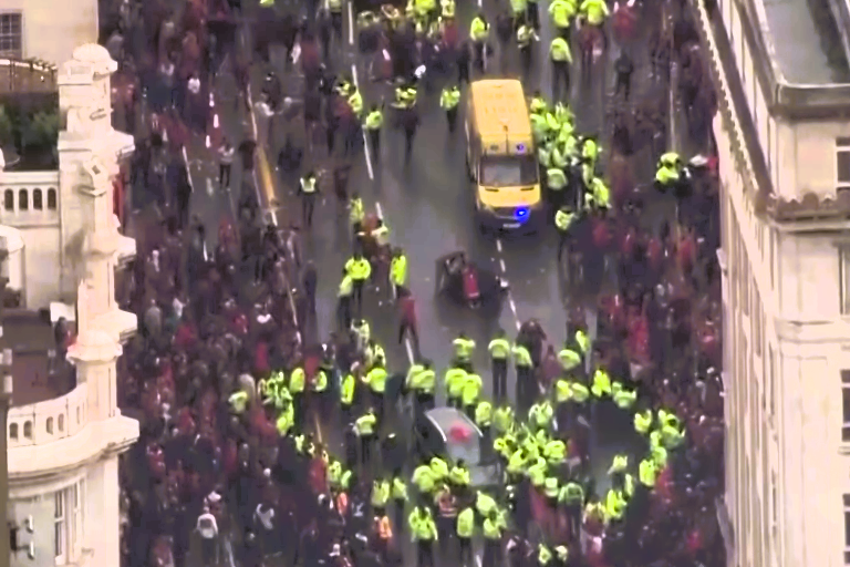 Aerial view of a yellow-jacketed police forming a cordon within a crowd.