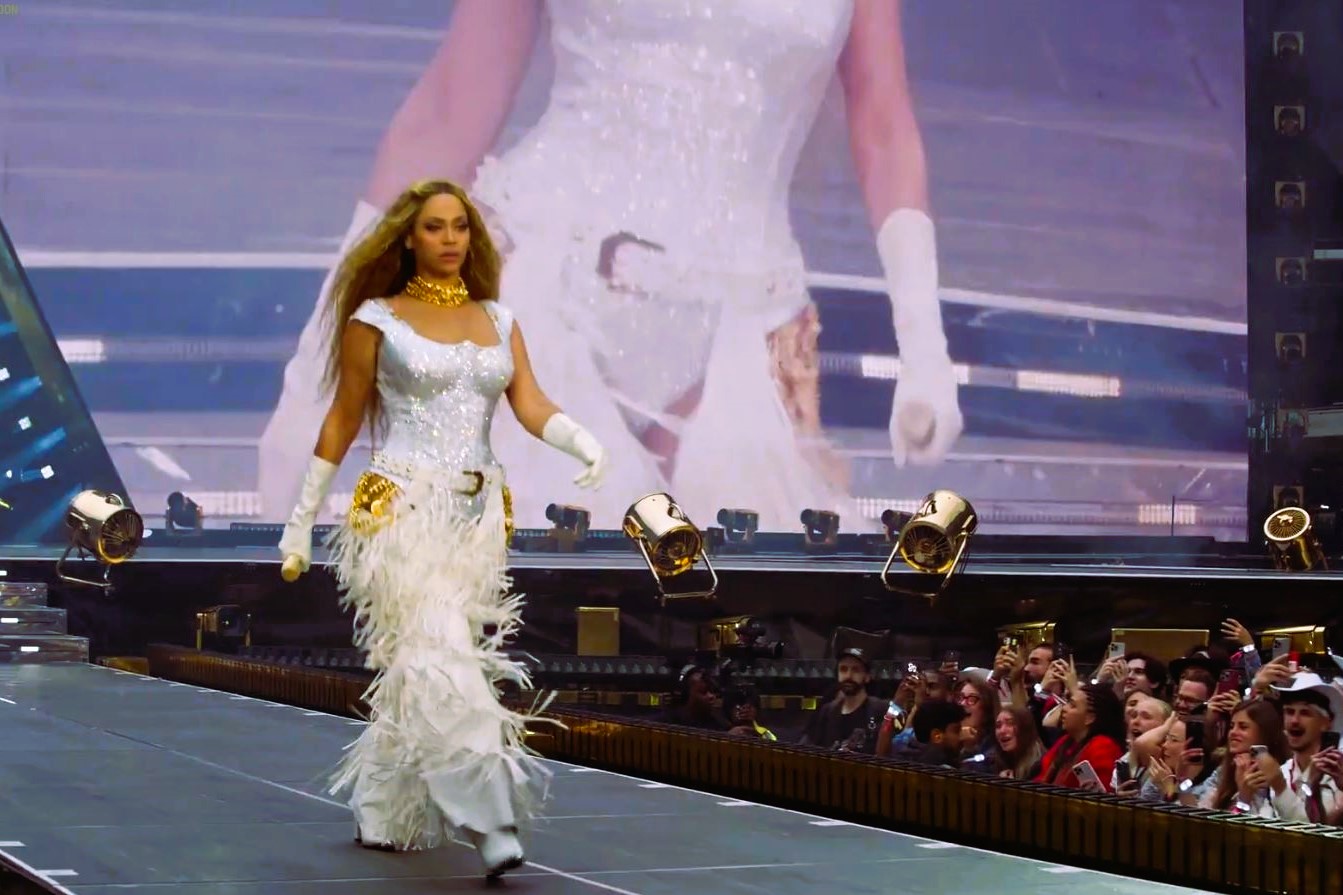 Beyonce marches along a stage catwalk as photographers stare from below.