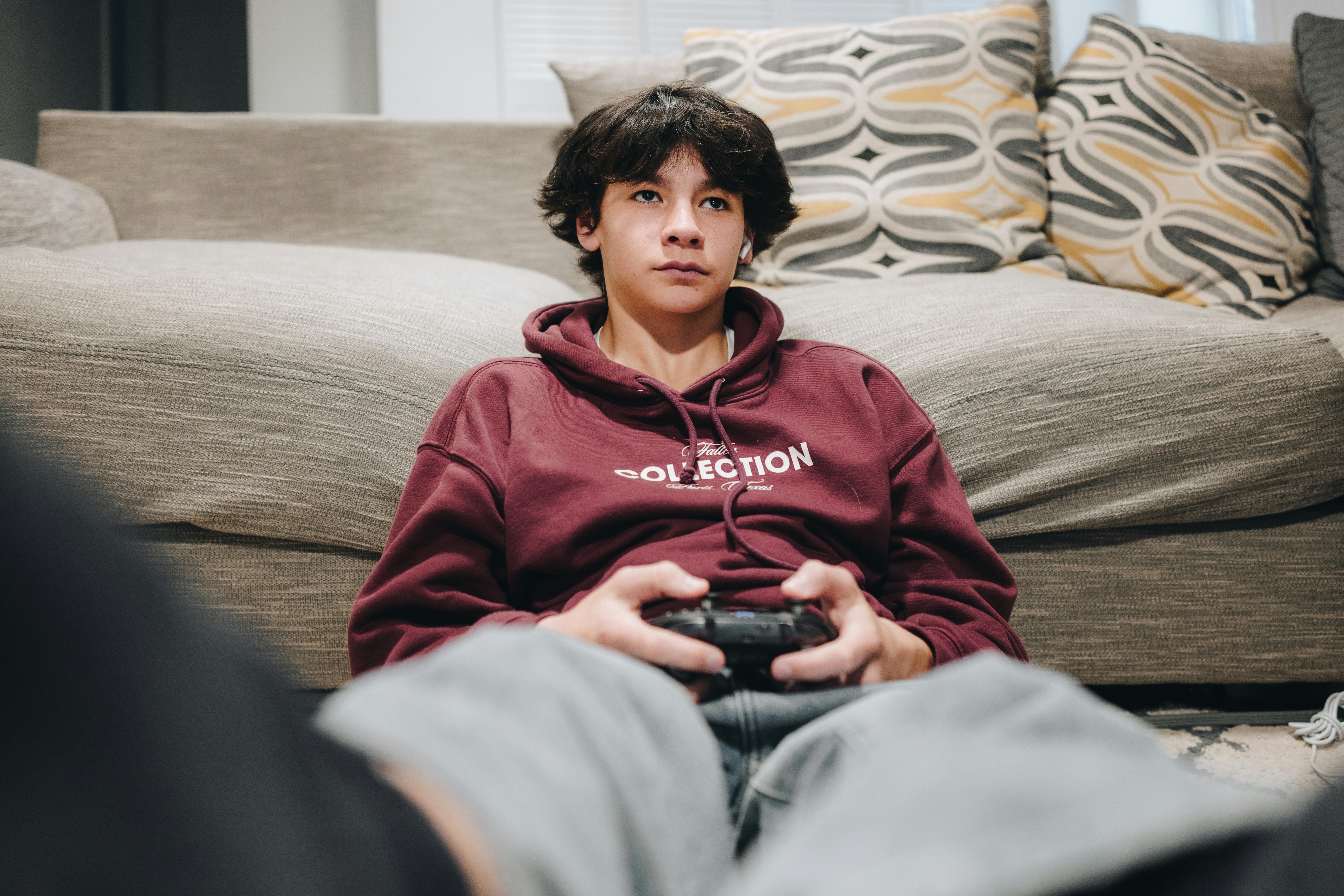 A teenager slumped against a sofa plays a video game