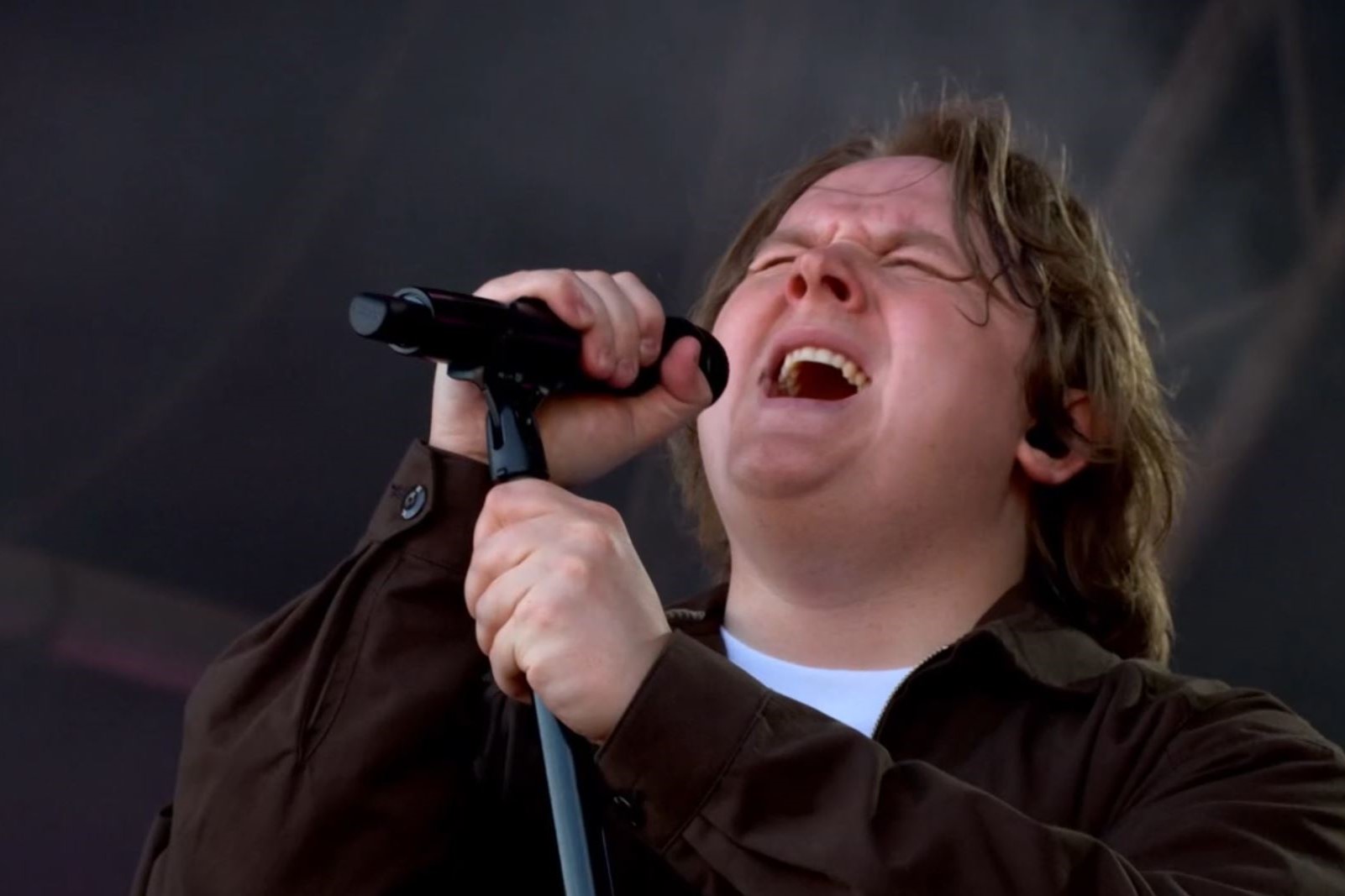 Lewis Capaldi sings with eyes closes, holding a mic and its stand