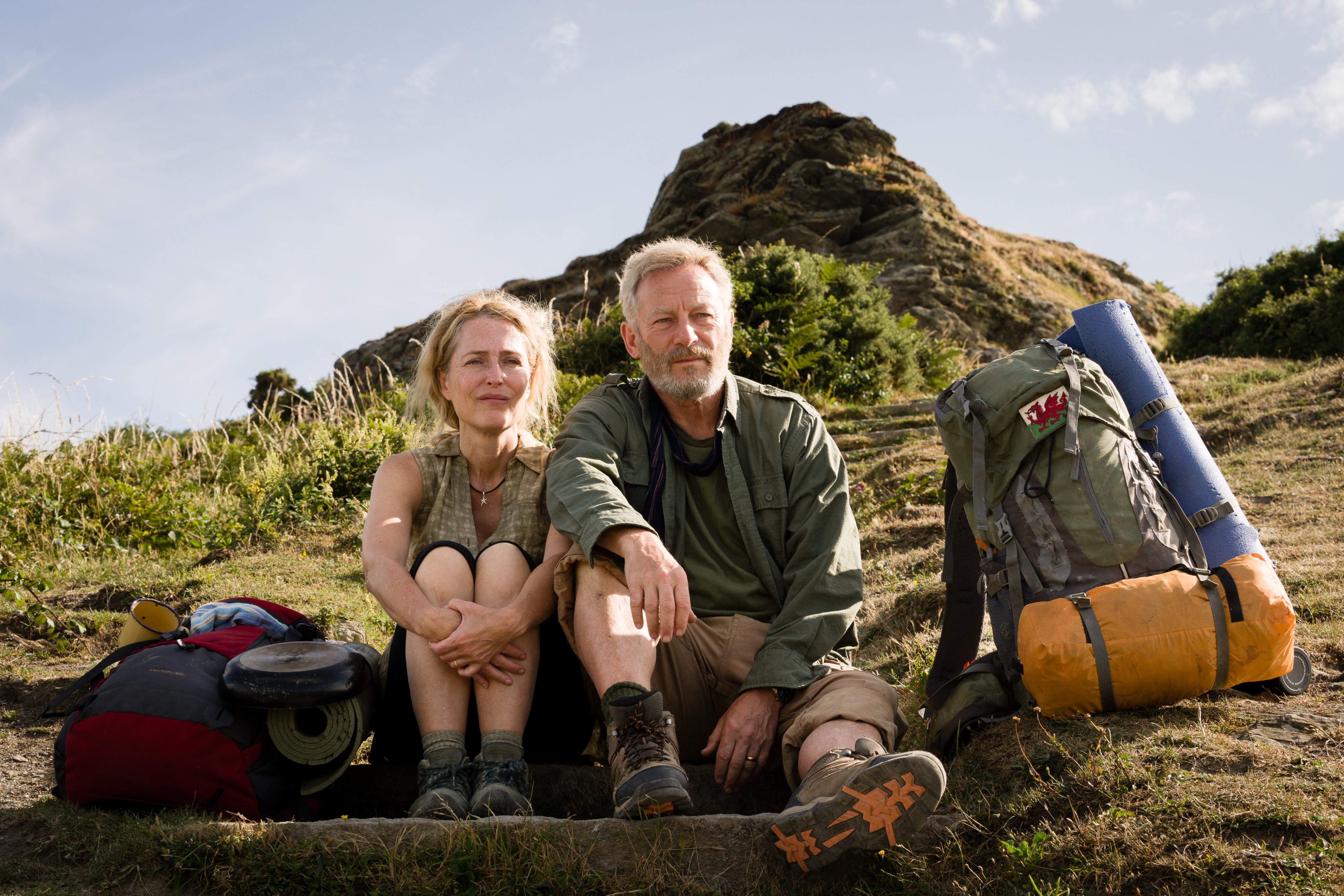 A hiking couple sit on the grass next to a pack.