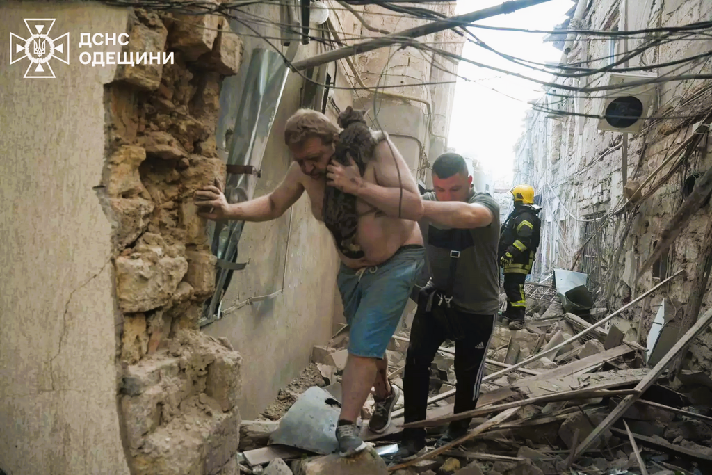 Amid a bombed alley, a victim is helped to walk by a rescue worker