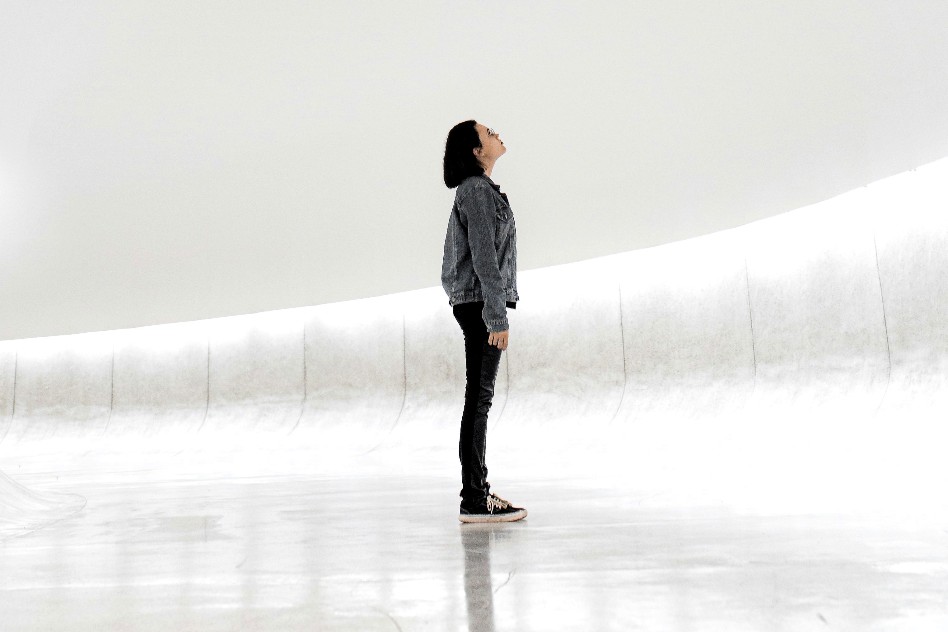 A woman stands against a sparse white background looking up.