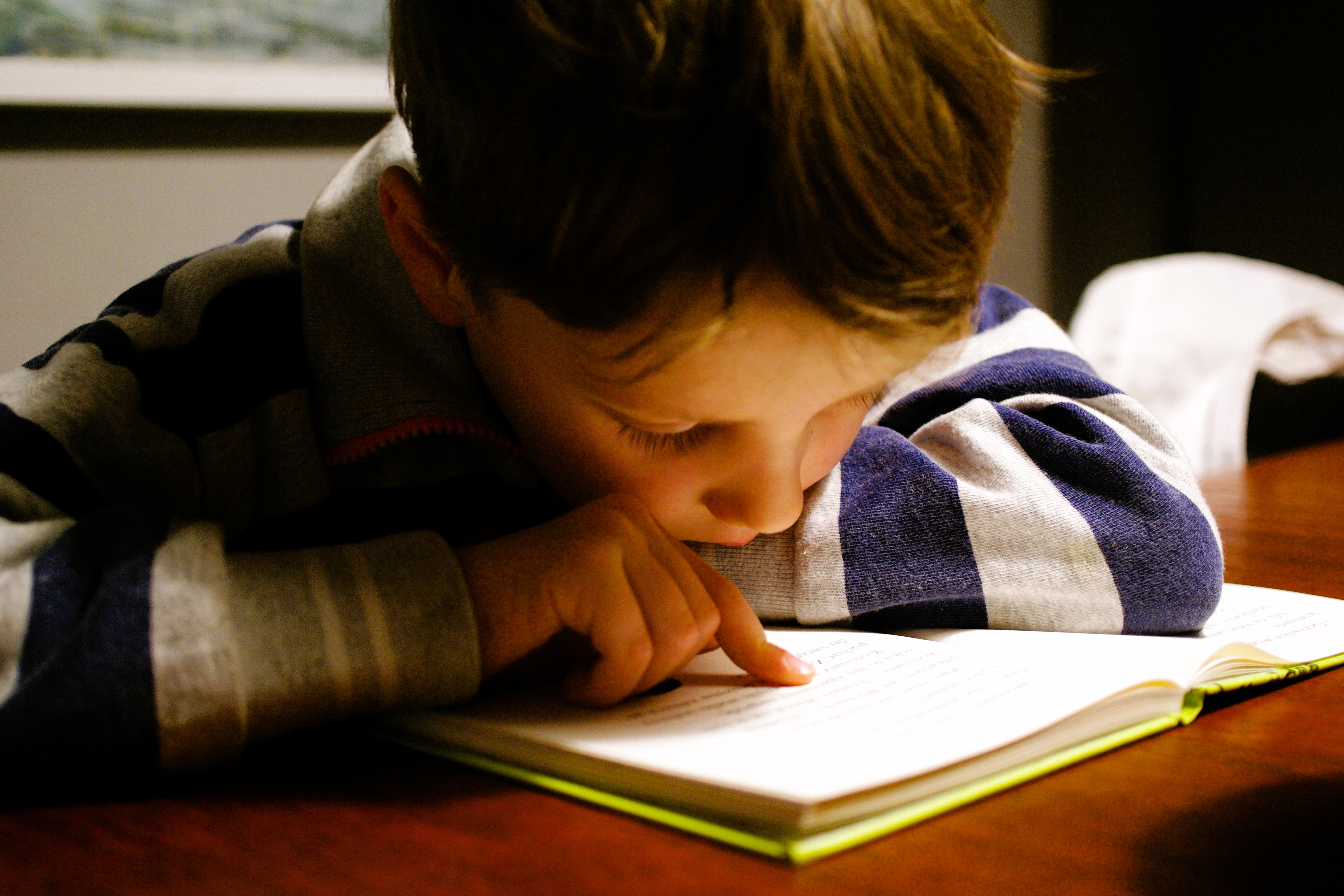 A young boy pores over a book tracing the lines with a finger.