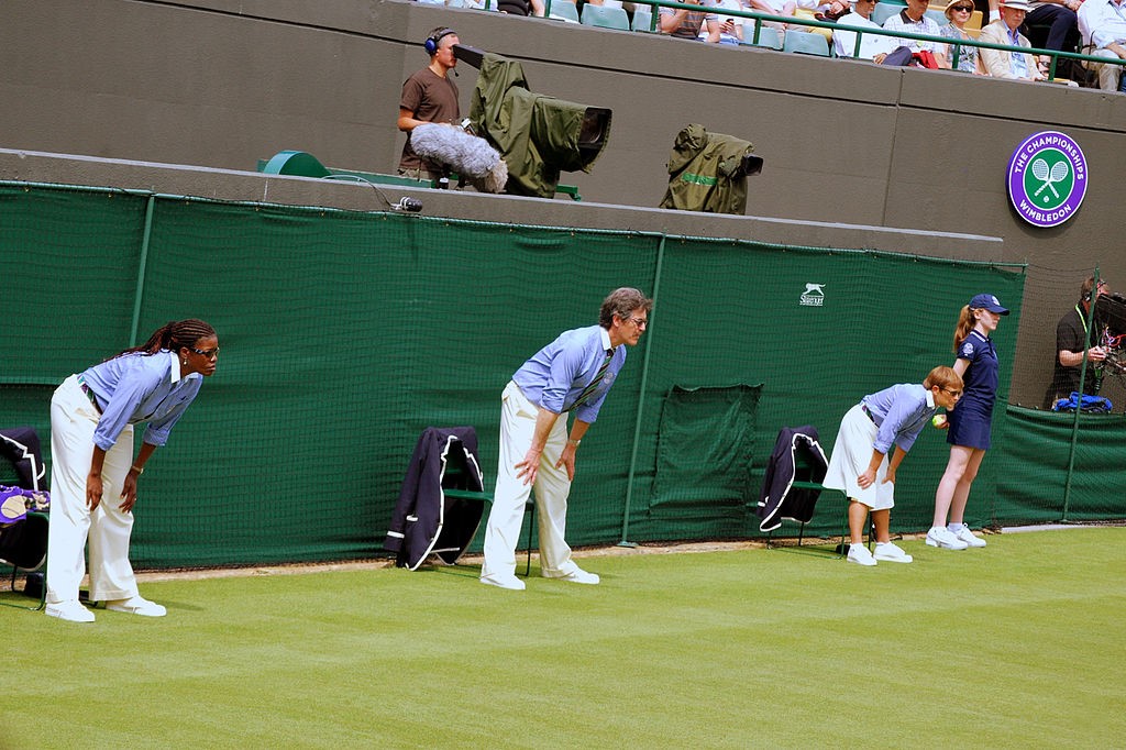 Tennis line judges stand and lean forward with hands on knees