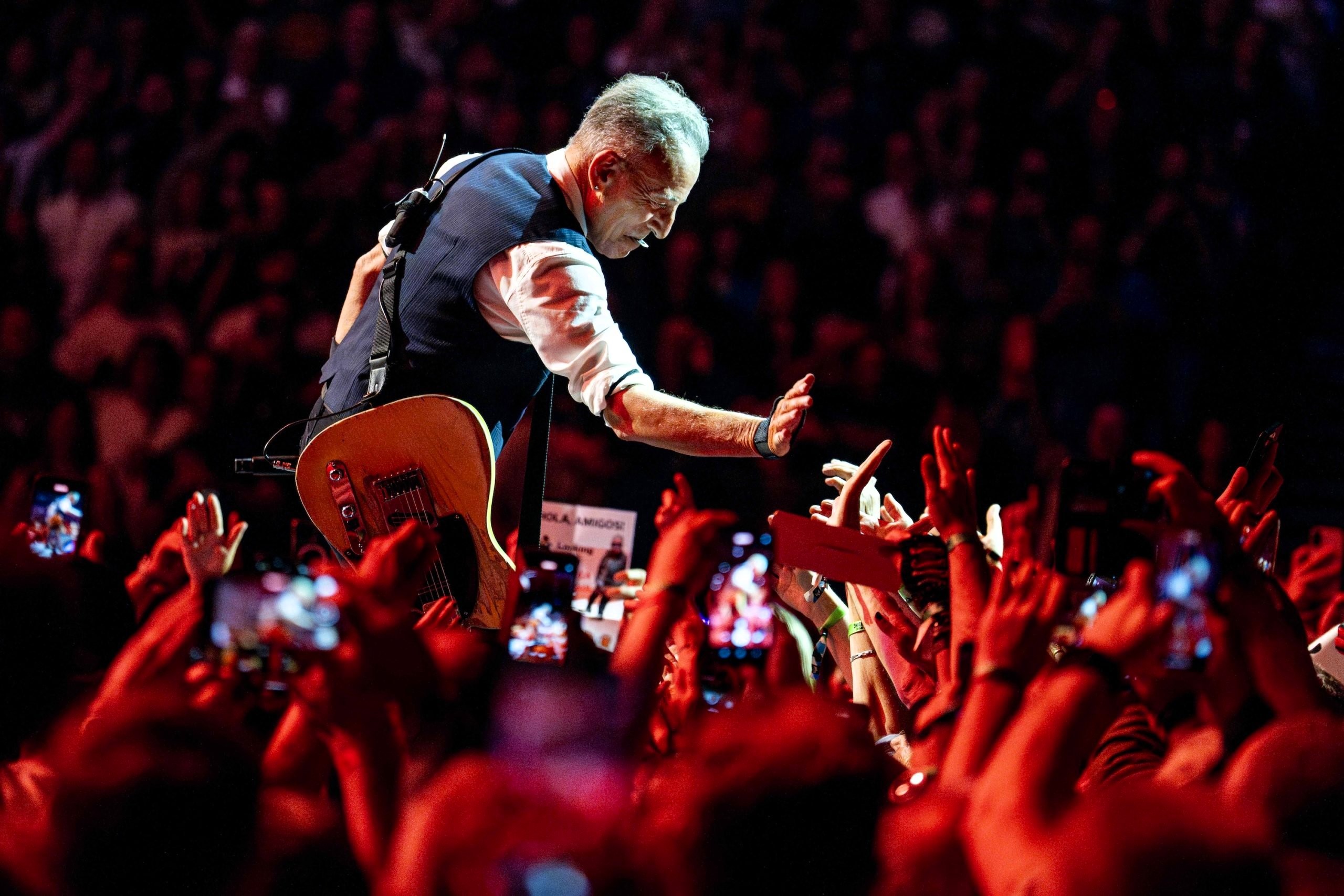 Bruce Springsteen crouches down and holds a hand out to a sea of outstretched hands