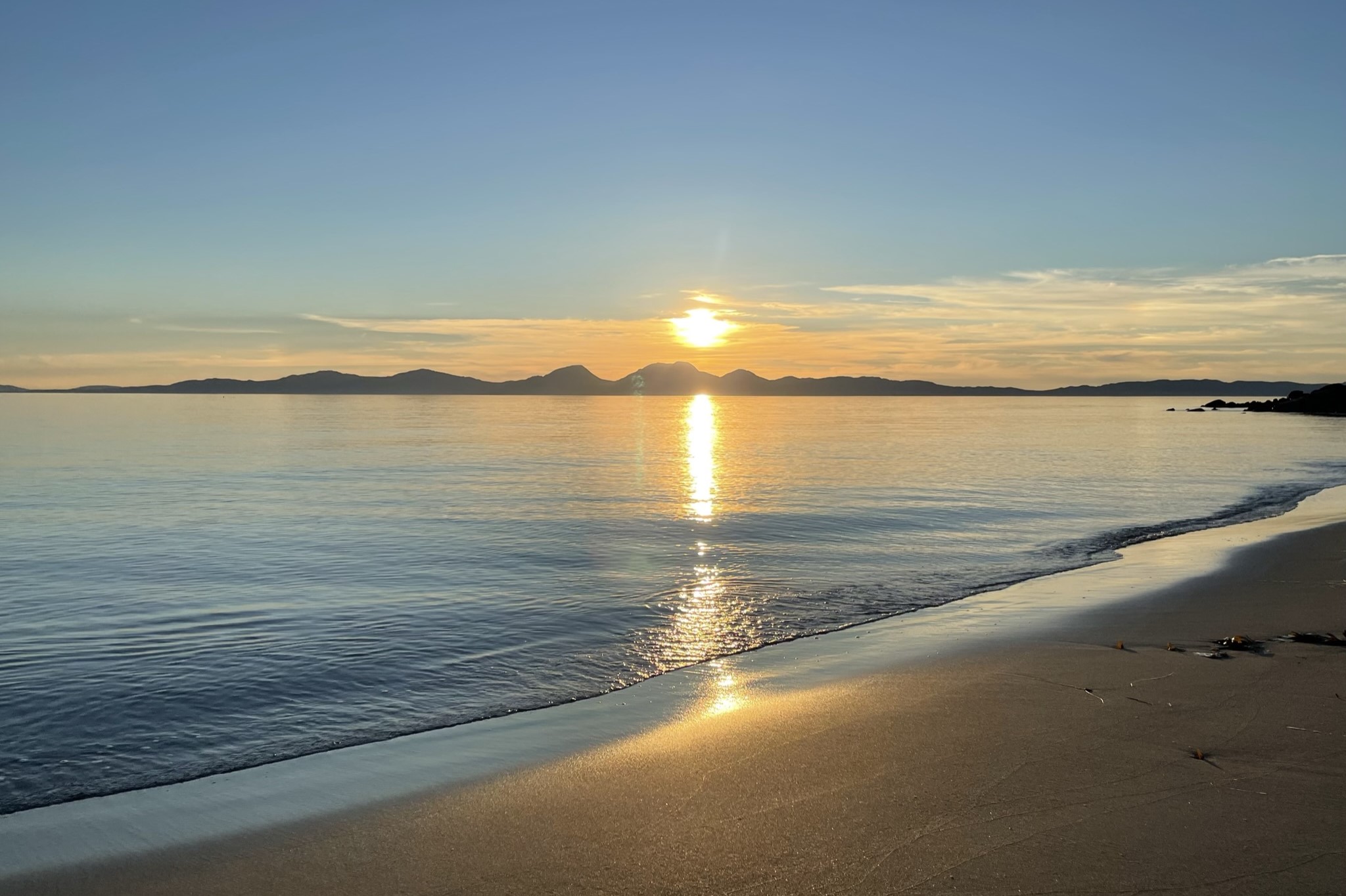 A sunset over an island casts golden light on the sea and a beach.