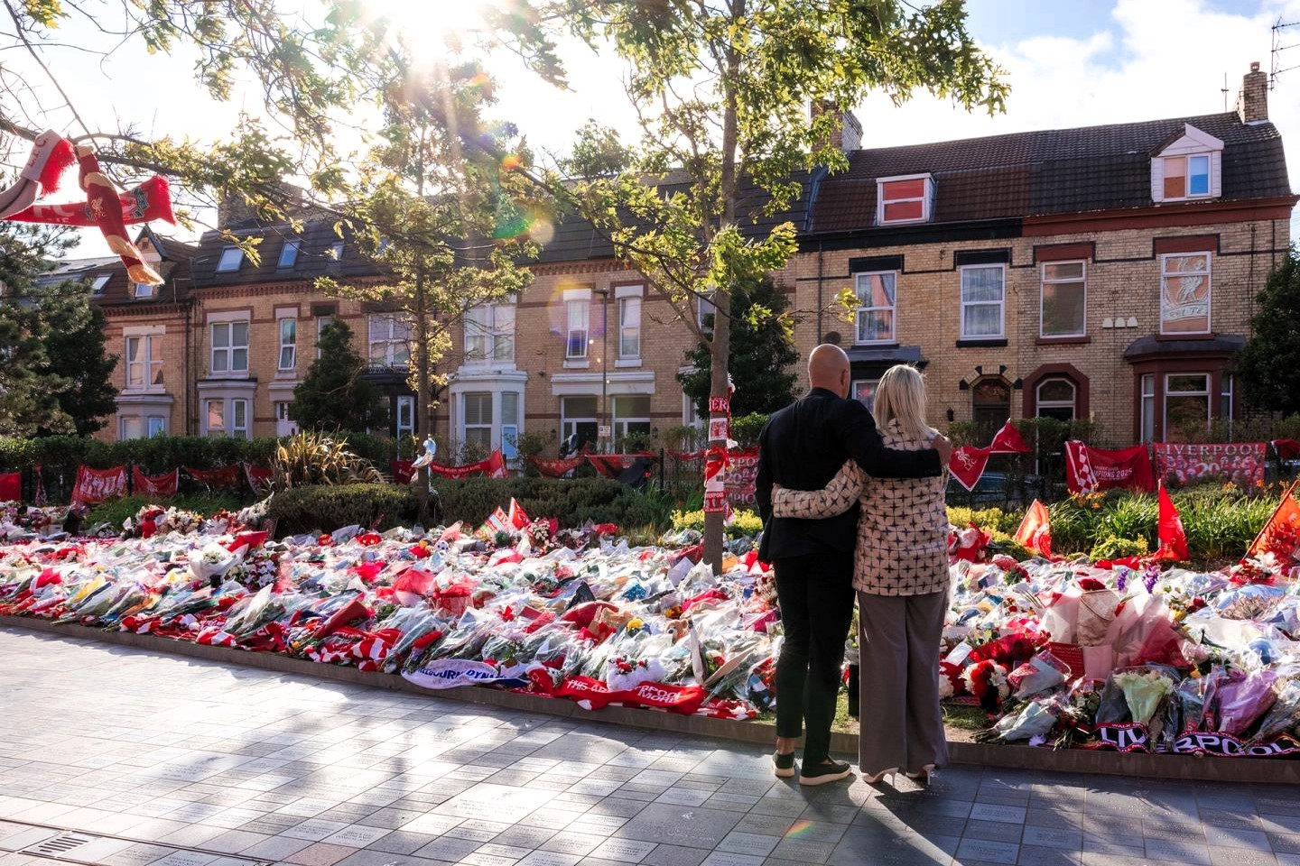 A couple hold each other as they look at floral tributes on the ground
