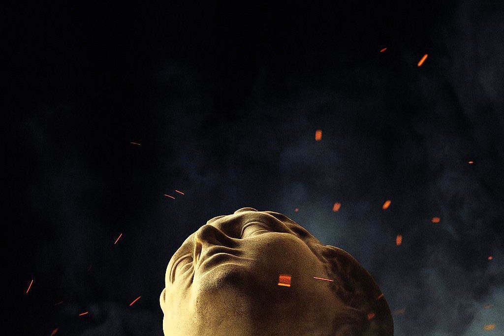the head of a classical statue looks up amid embers around it.