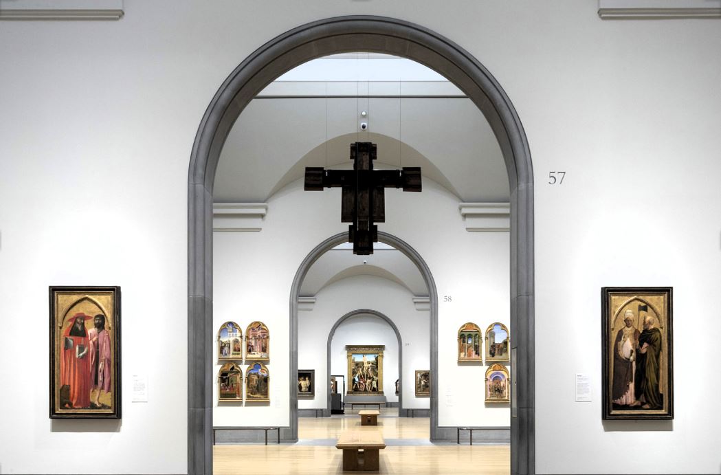 An art gallery arch reveals a suspended crucifix and other paintings in a distant room