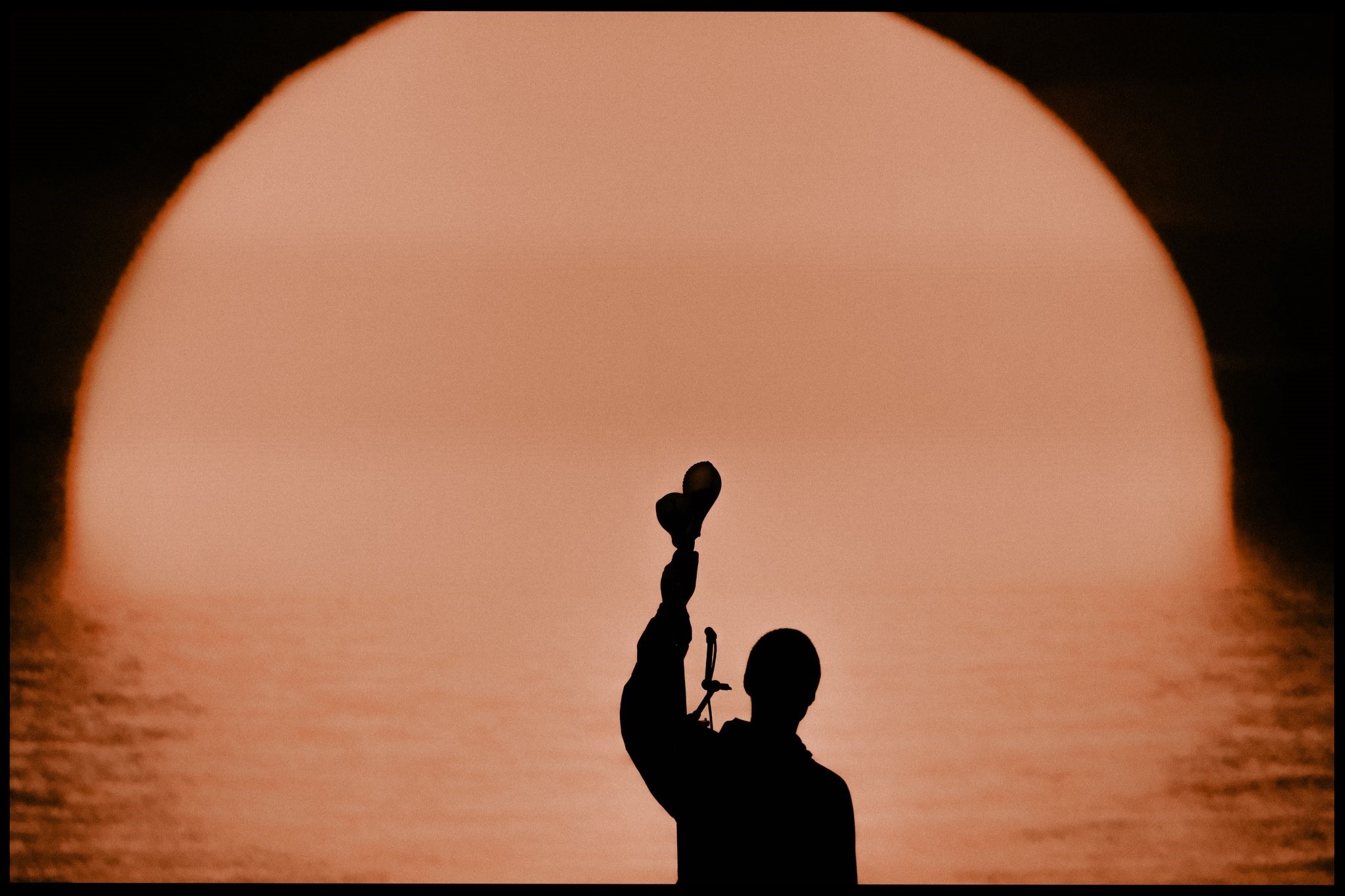 A silhouette of a musician holding up shakers.