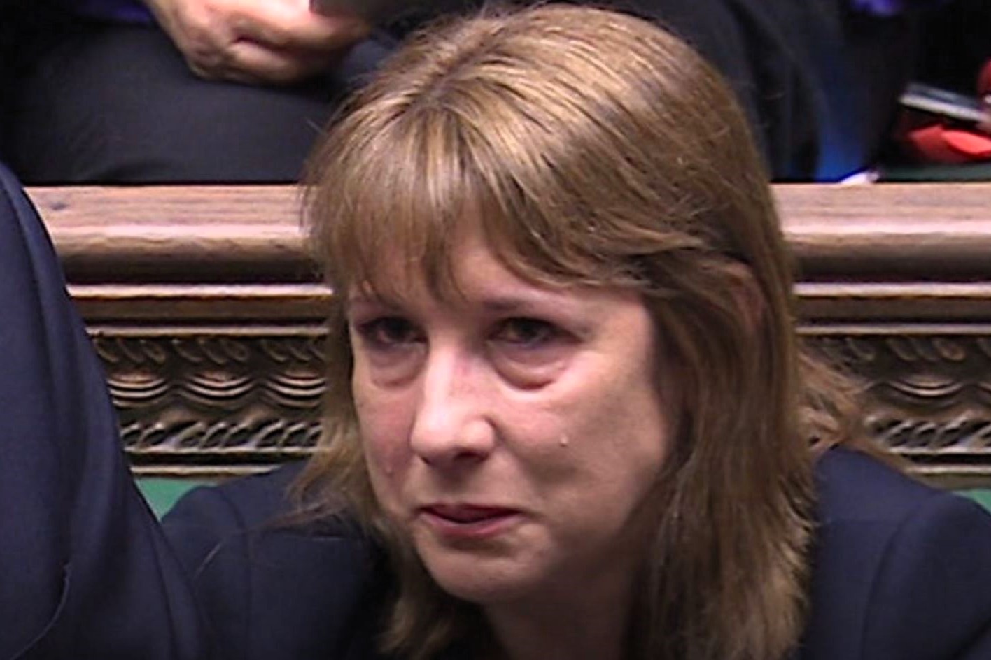 A woman sits and holds back a tear.