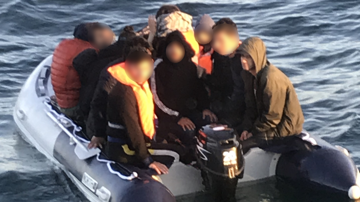 A people sumggler steers an overcrowded small boat.