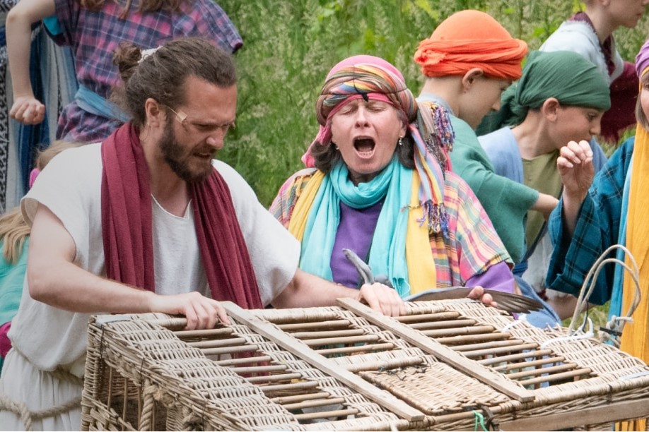 An outdoor theatrical setting shows Jesus with a basket.