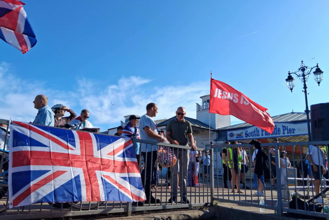 A Union Jack is draped over a railing, next to a red flag saying Jesus.