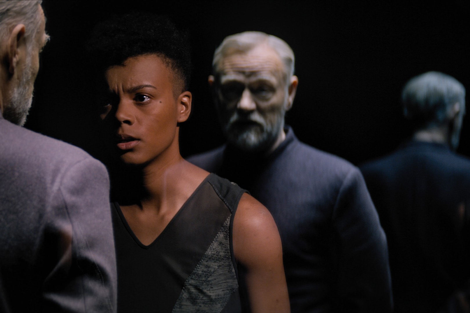 A woman confronts a man whose clone stands behind her.