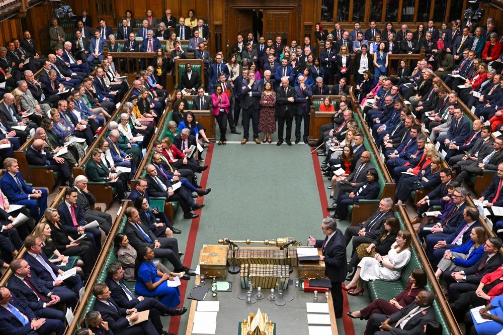 MPs sit and stand in a crowded parliament.