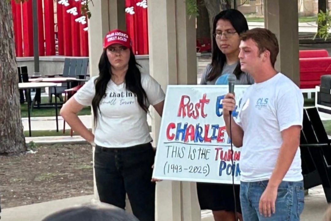 Mourning students at a vigil hold a sign about Charlie Kirk.