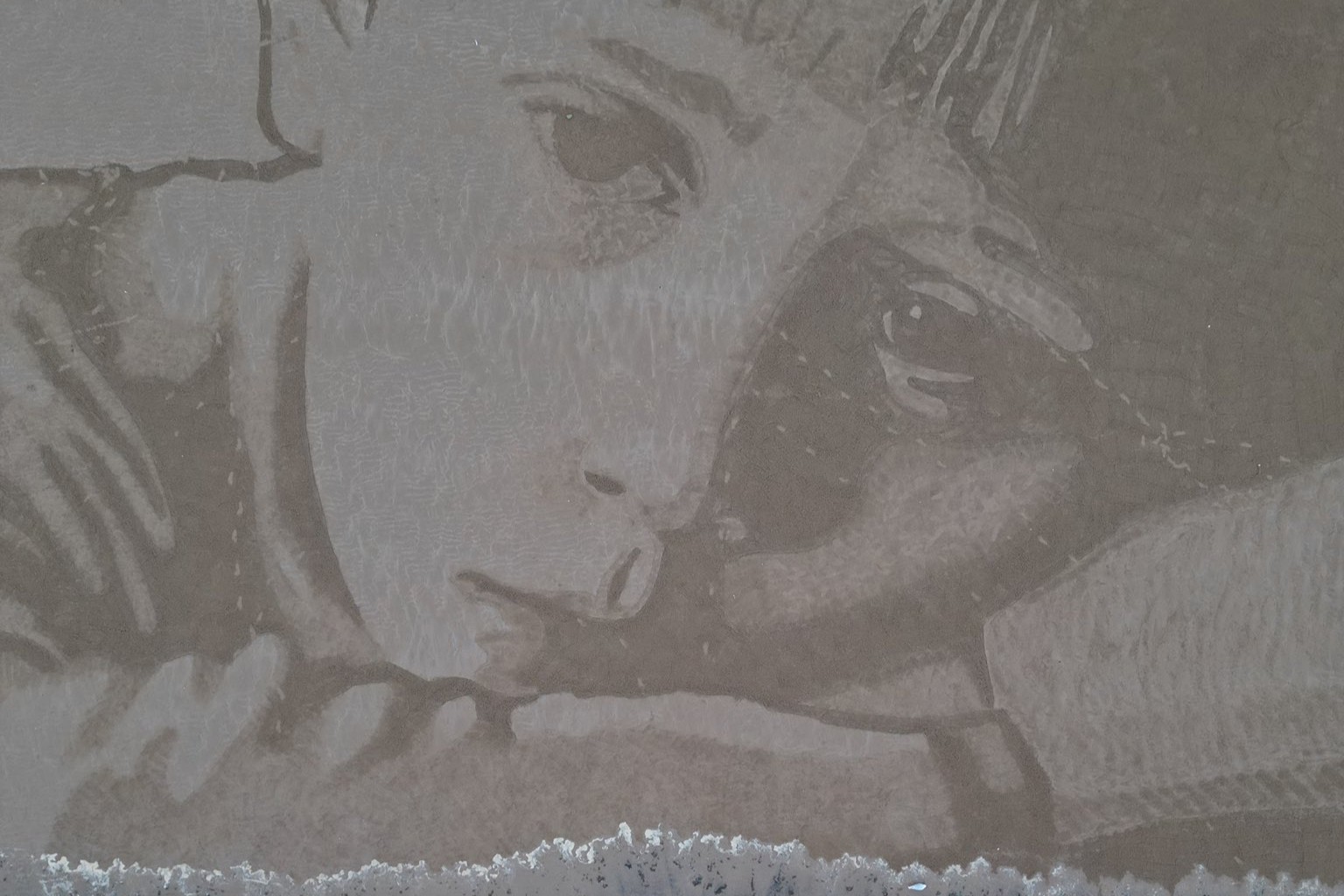 A sand drawing shows an unhappy child's face with the tide coming in from below