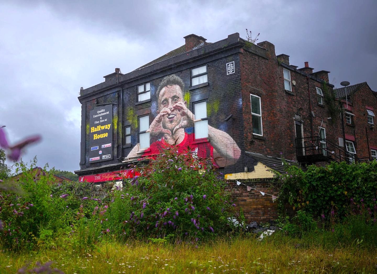 A mural on a side of a pub shows a footballer making a heart sign.