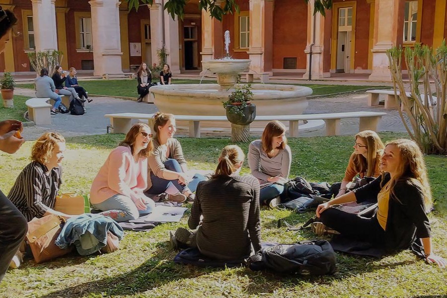 Students sit on the grass in front of a fountain.