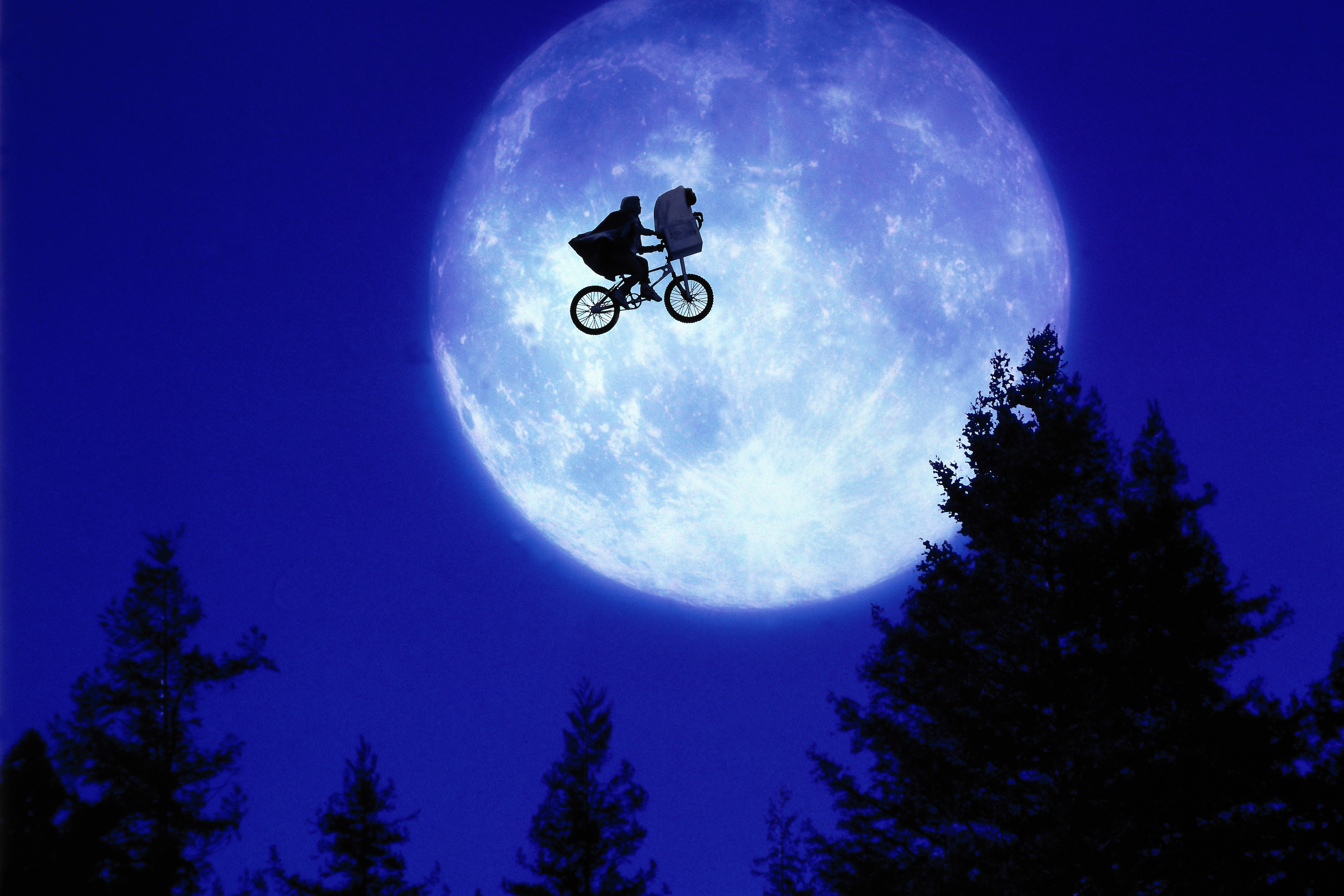 A child and E.T. ride a BMX bike across a moon lit sky.