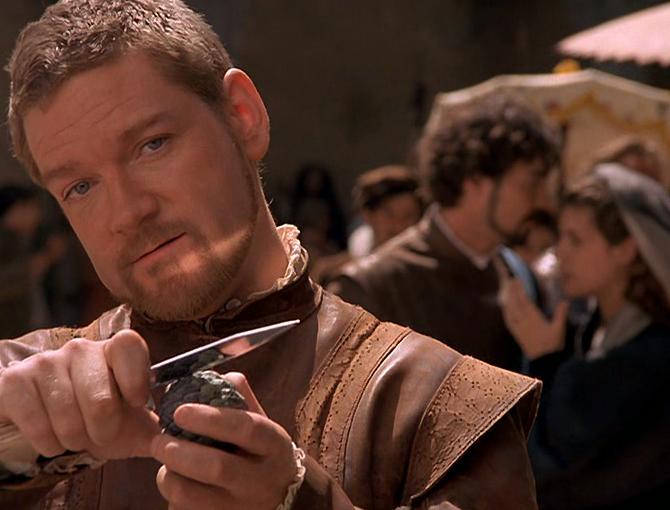 An Elizabethan man holds a dagger up while grinning.