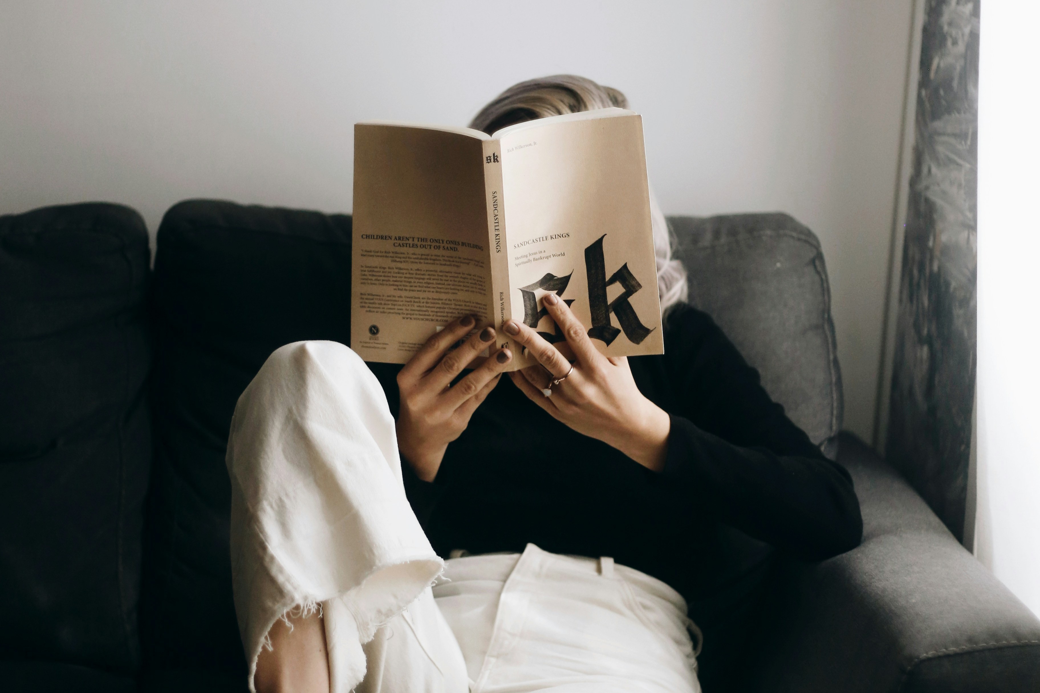   A reader sits on a sofa with a raised leg and holds a book