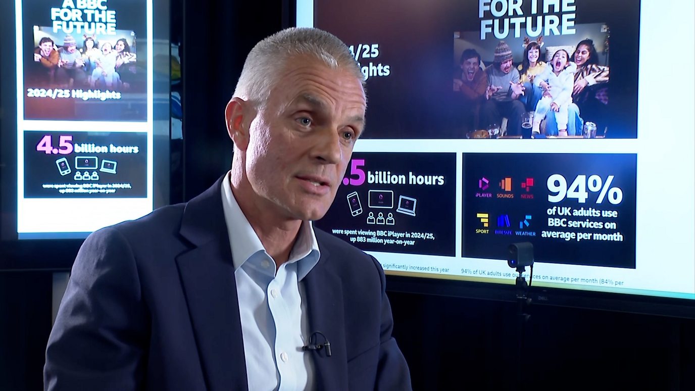TIm Davie, sits in an interview in front of screens showing facts about the BBC