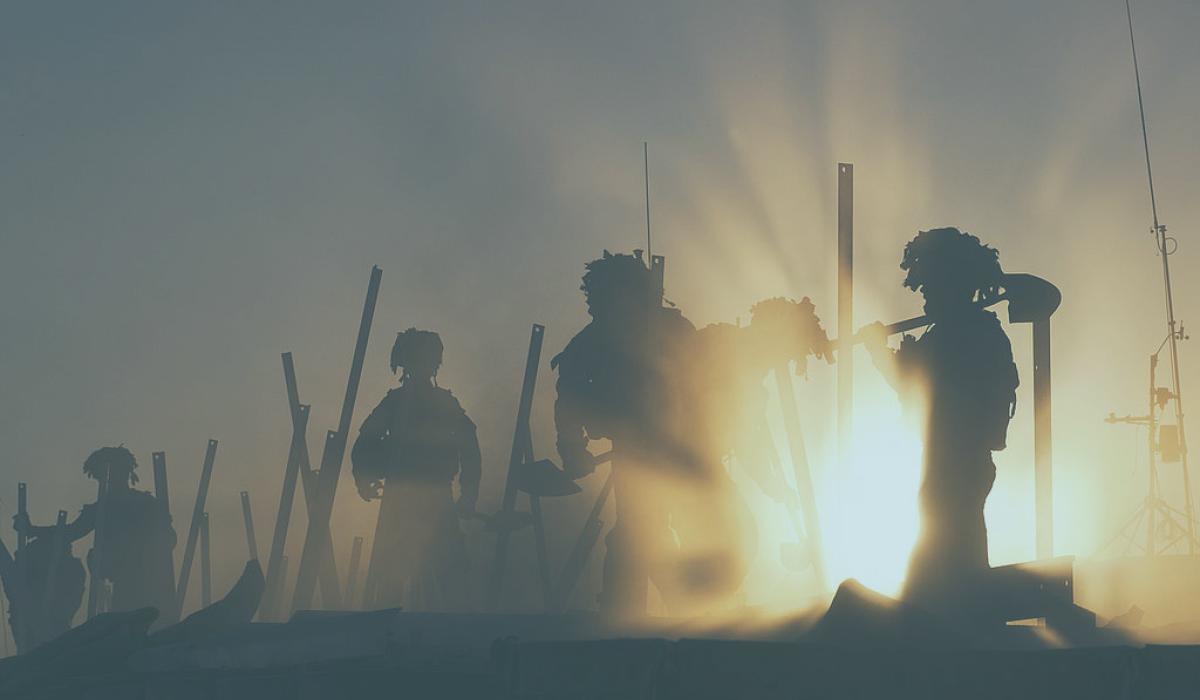 Soldiers silhouetted by dust and sunshine work at a fence with tools.