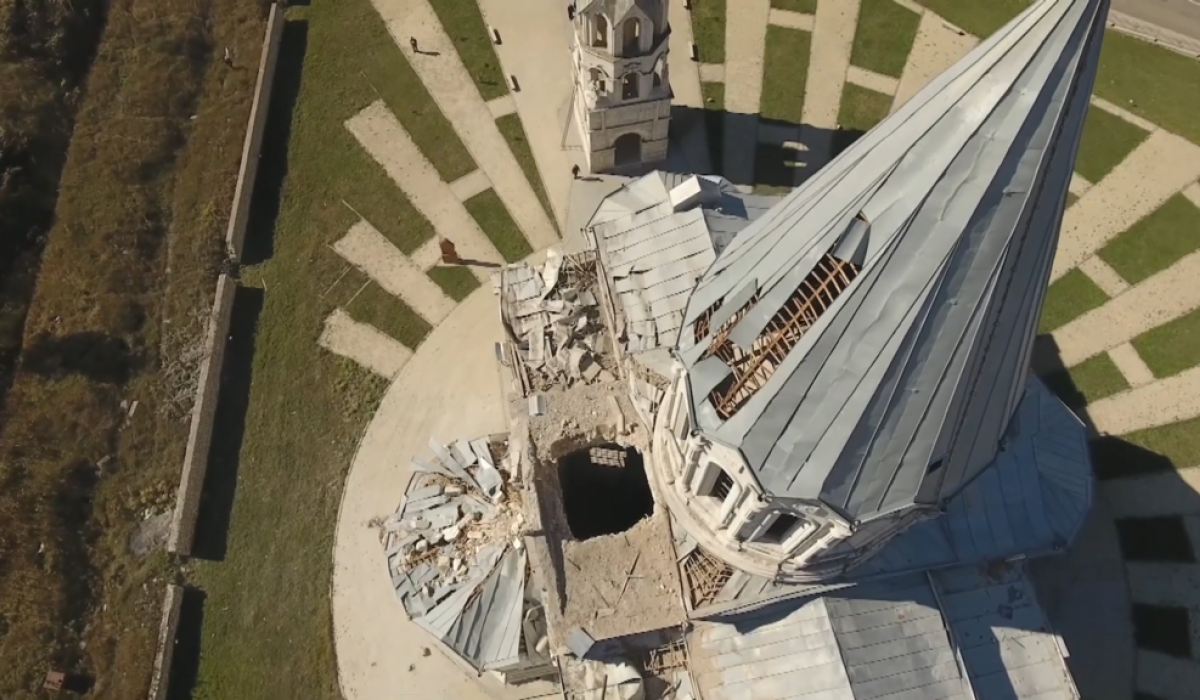 An aerial view looking down the damaged spire of a cathederal to a holes in the roof caused by shelling.