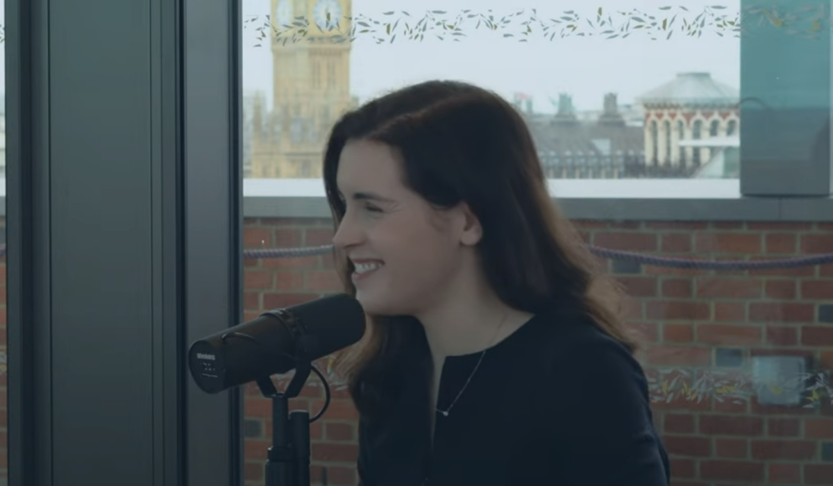 A woman smiles as she speaks into a microphone. In the background is Big Ben.
