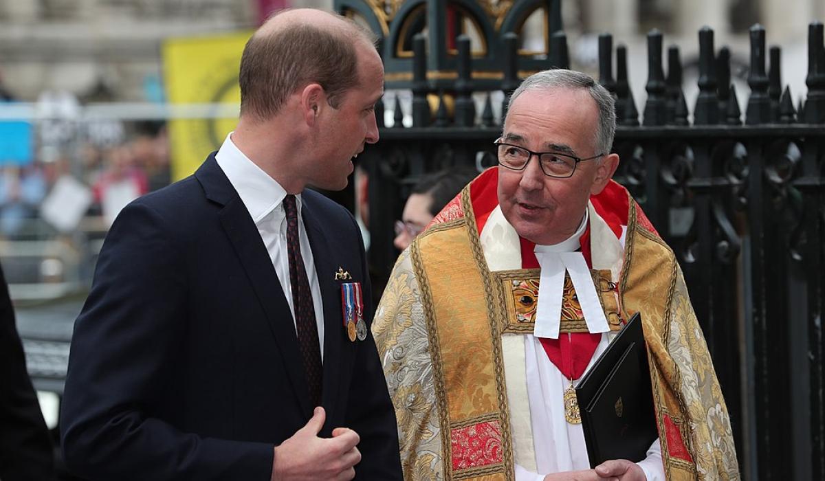 A young man wearing a dark suit talks to a minister wearing regalia.