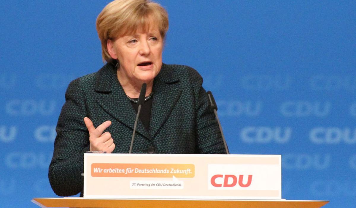 A politician stands a labelled lectern speaking and gesticulating with a hand.