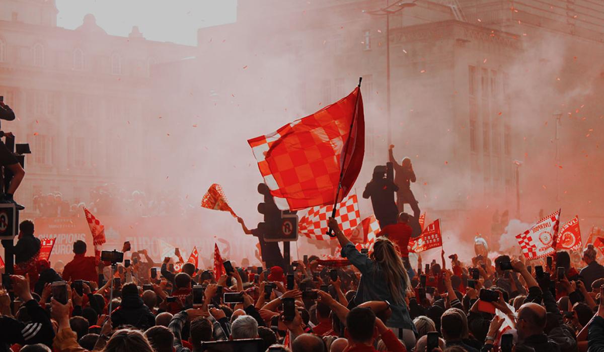 Silouhetted by red flare smoke, celebrating footballs wave red flags.