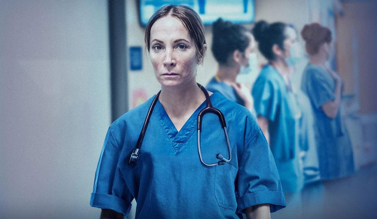 A doctor in blue scrubs stands looking exhausted.