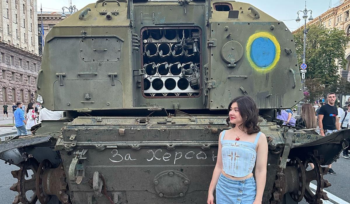 A woman stands at the back of an armoured military vehicle, the door of which is open.