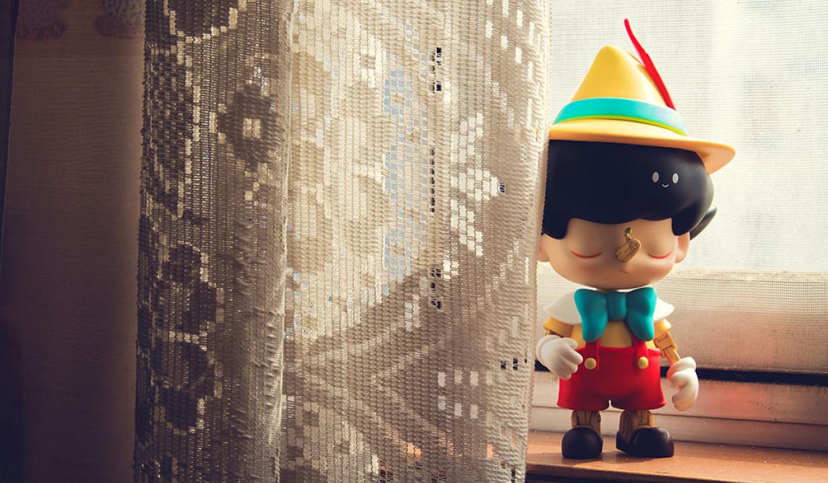 A Pinnochio figure stands on a window sill beside some net curtains.
