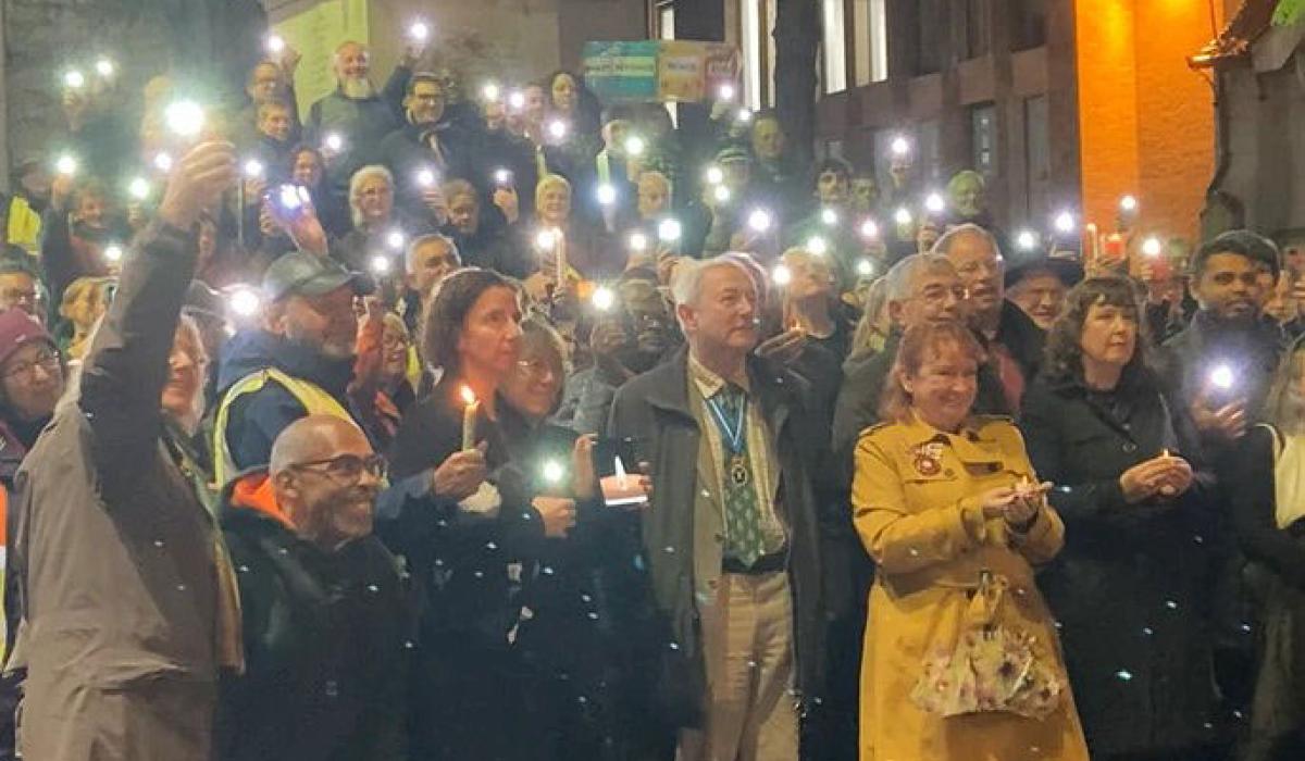 An outdoor vigil is lit by people holding up mobile phone lights.