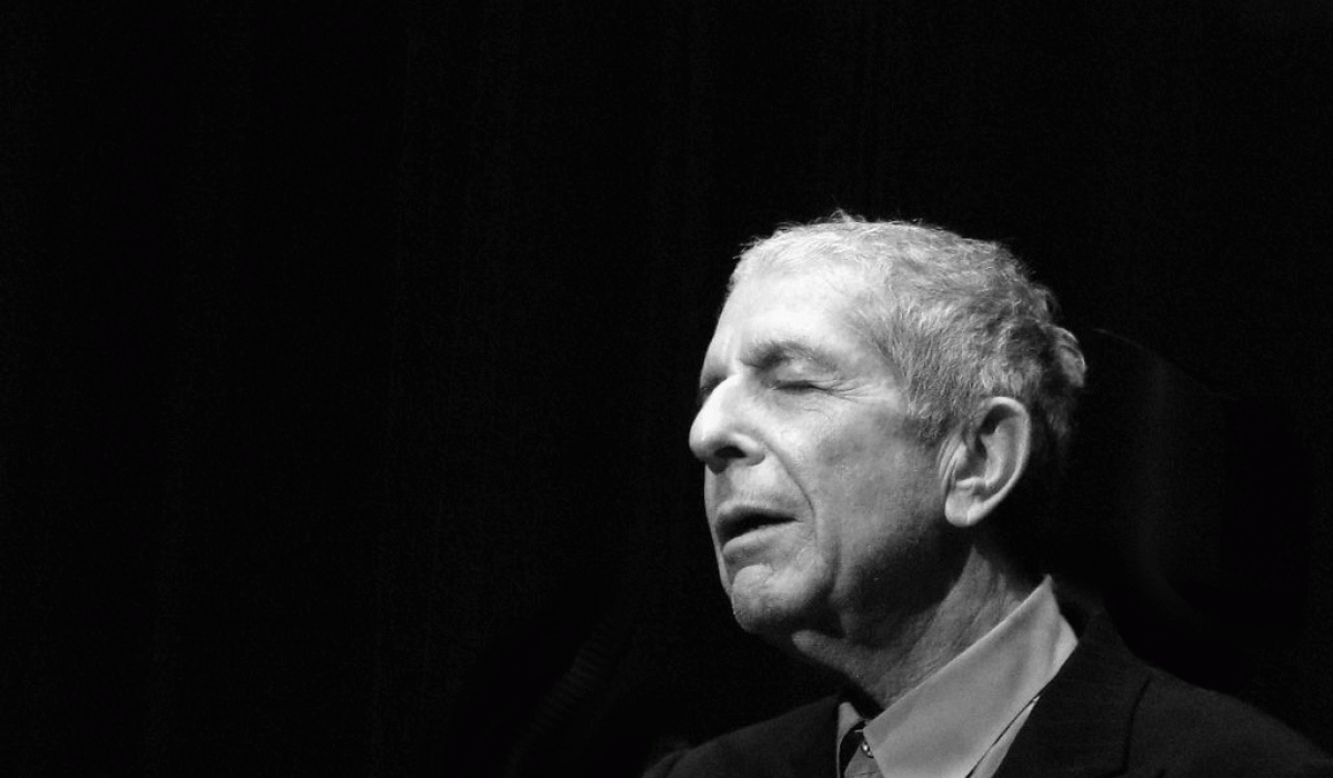 A black and white photo shows, singer Leonard Cohen to the right hand side, eyes closed and head inclined slightly upwards.